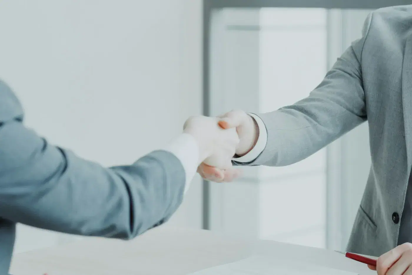 Two people shaking hands across a desk after an interview