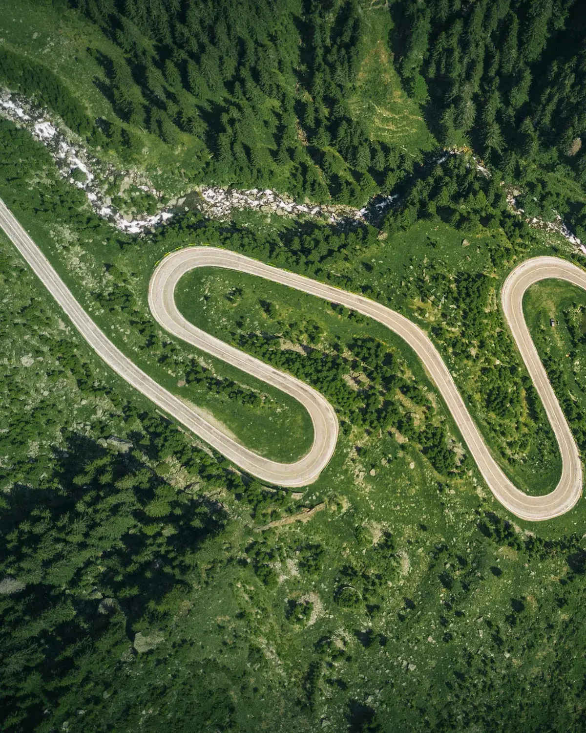 A mountain road winding back and forth through green forest, seen from above