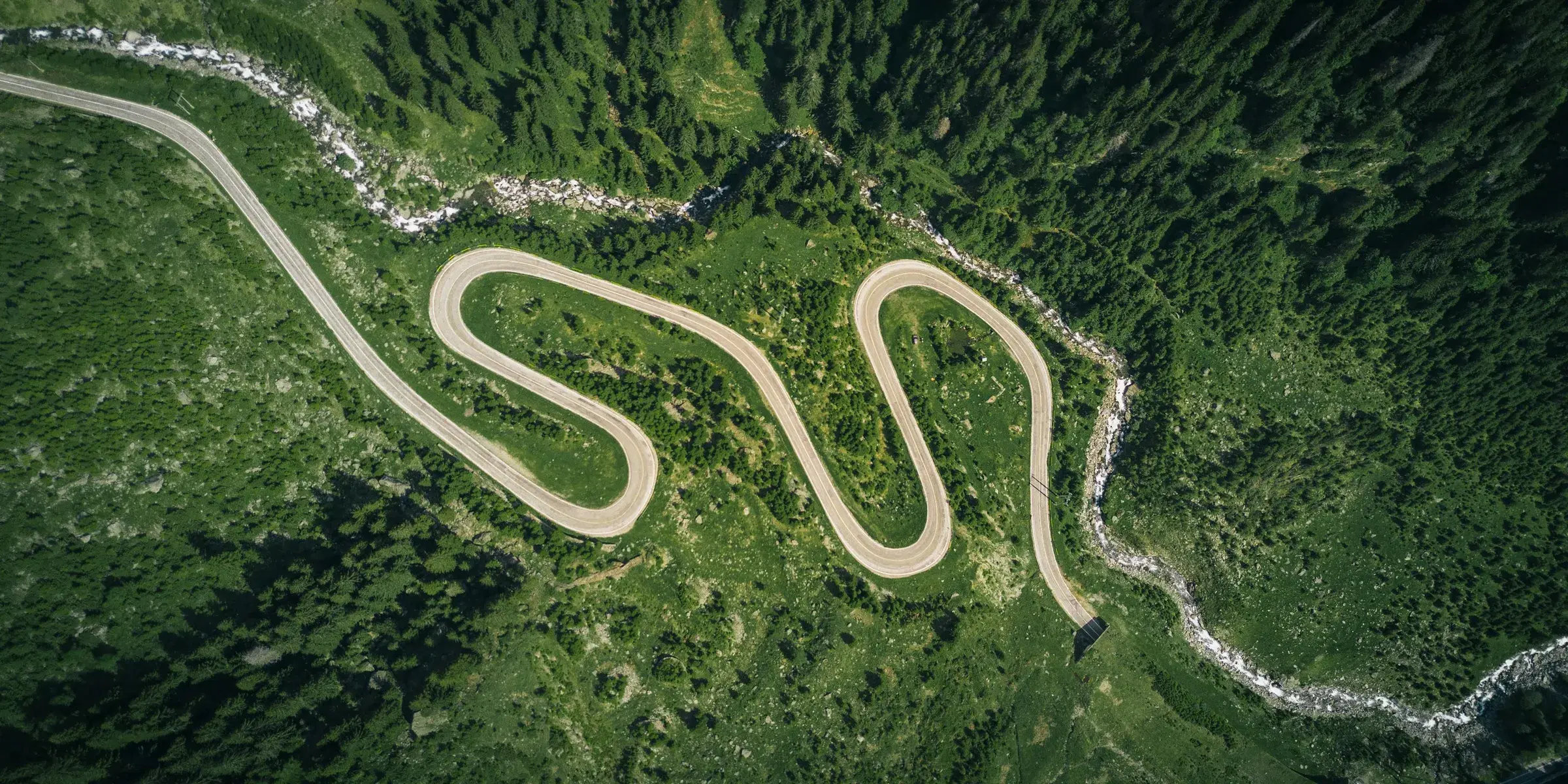 A mountain road winding back and forth through green forest, seen from above